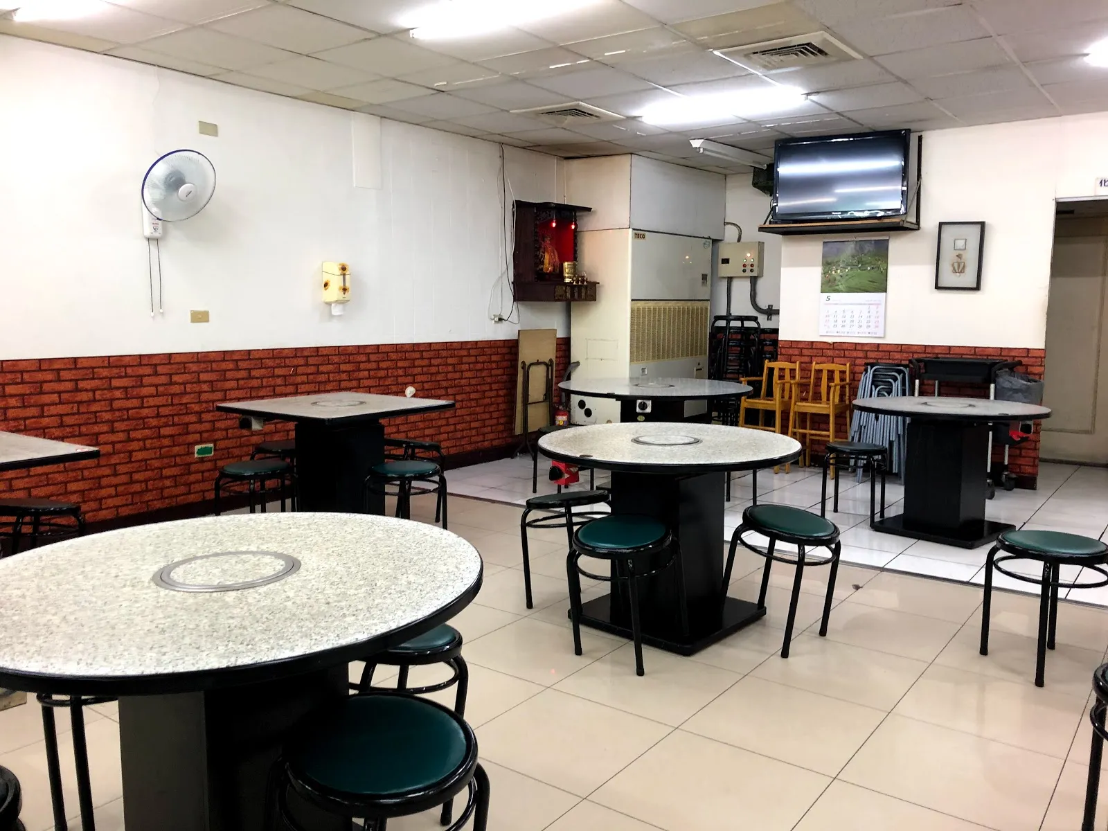 店內用餐區，白色磨石子圓桌中央嵌著爐口，四周擺著深綠色圓凳，牆面下半部貼著紅磚