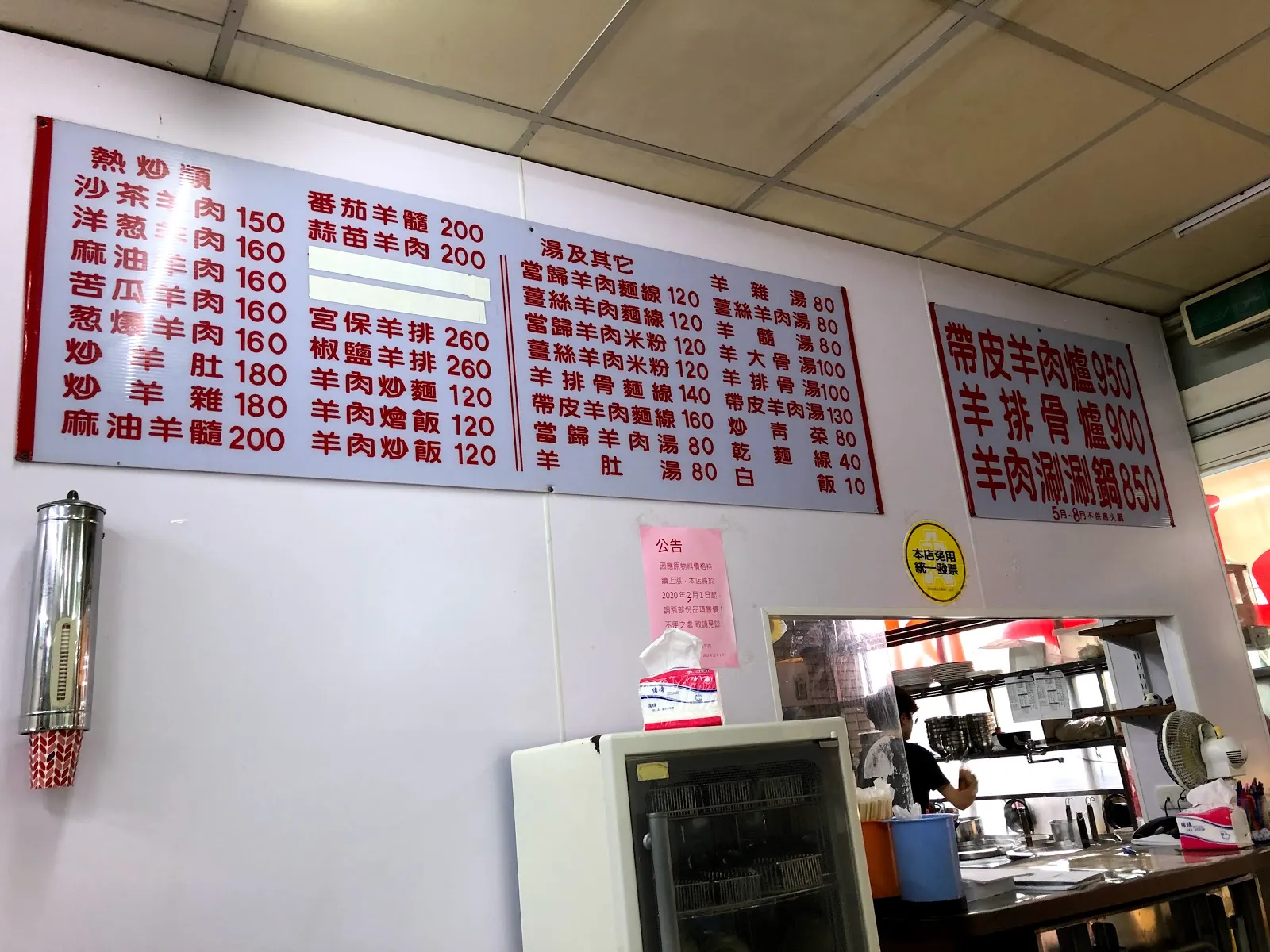 店內牆上的大型菜單看板，紅字寫在白底上，右側特別標出帶皮羊肉爐 950、羊排骨爐 900、羊肉涮涮鍋 850，下方是廚房的開放式窗口