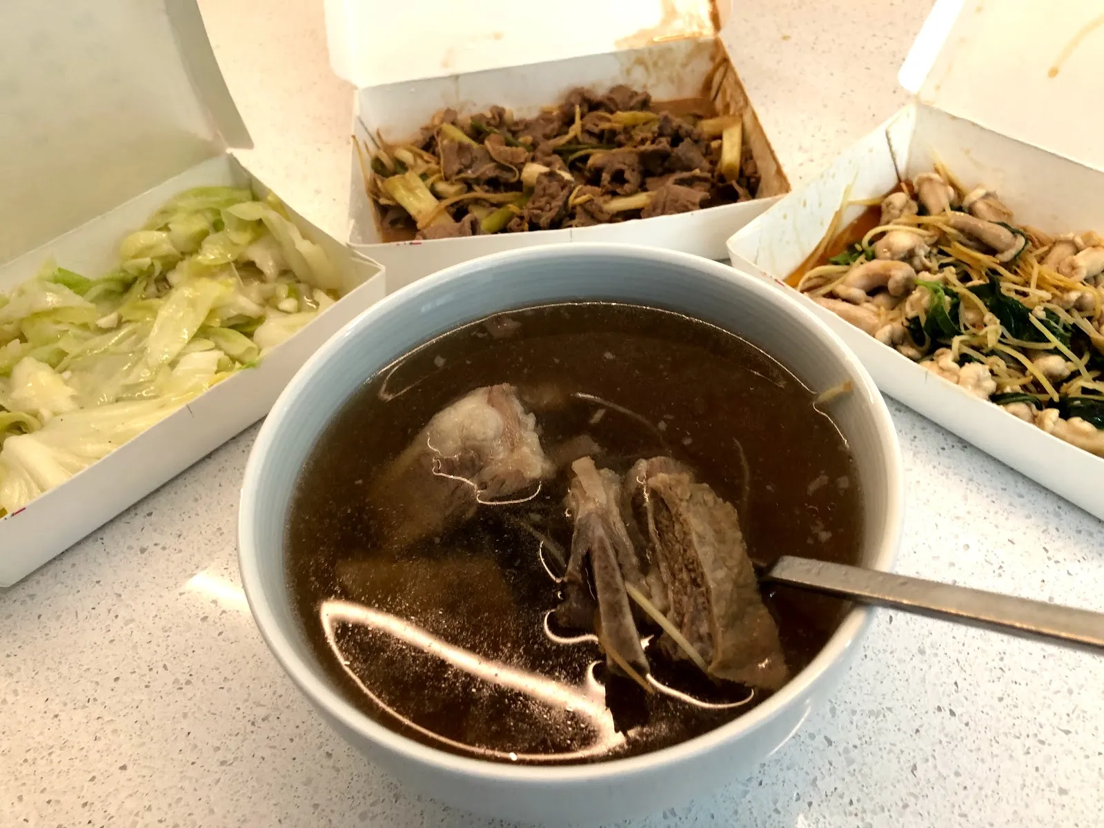 外帶回家的四樣菜攤在桌上，中間白瓷碗裡是深褐色的羊肉湯，周圍紙盒分別裝著炒高麗菜、蔥爆羊肉與薑絲炒羊雜