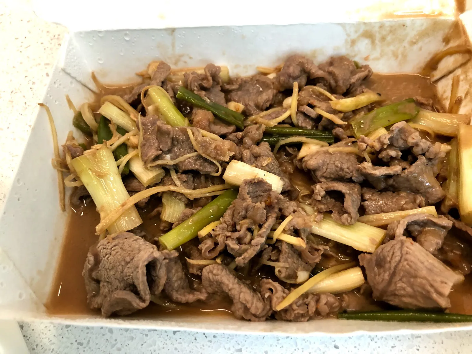 紙盒裡的蔥爆羊肉，薄切羊肉片與整段青蔥、薑絲一起拌炒，盒底積著醬汁
