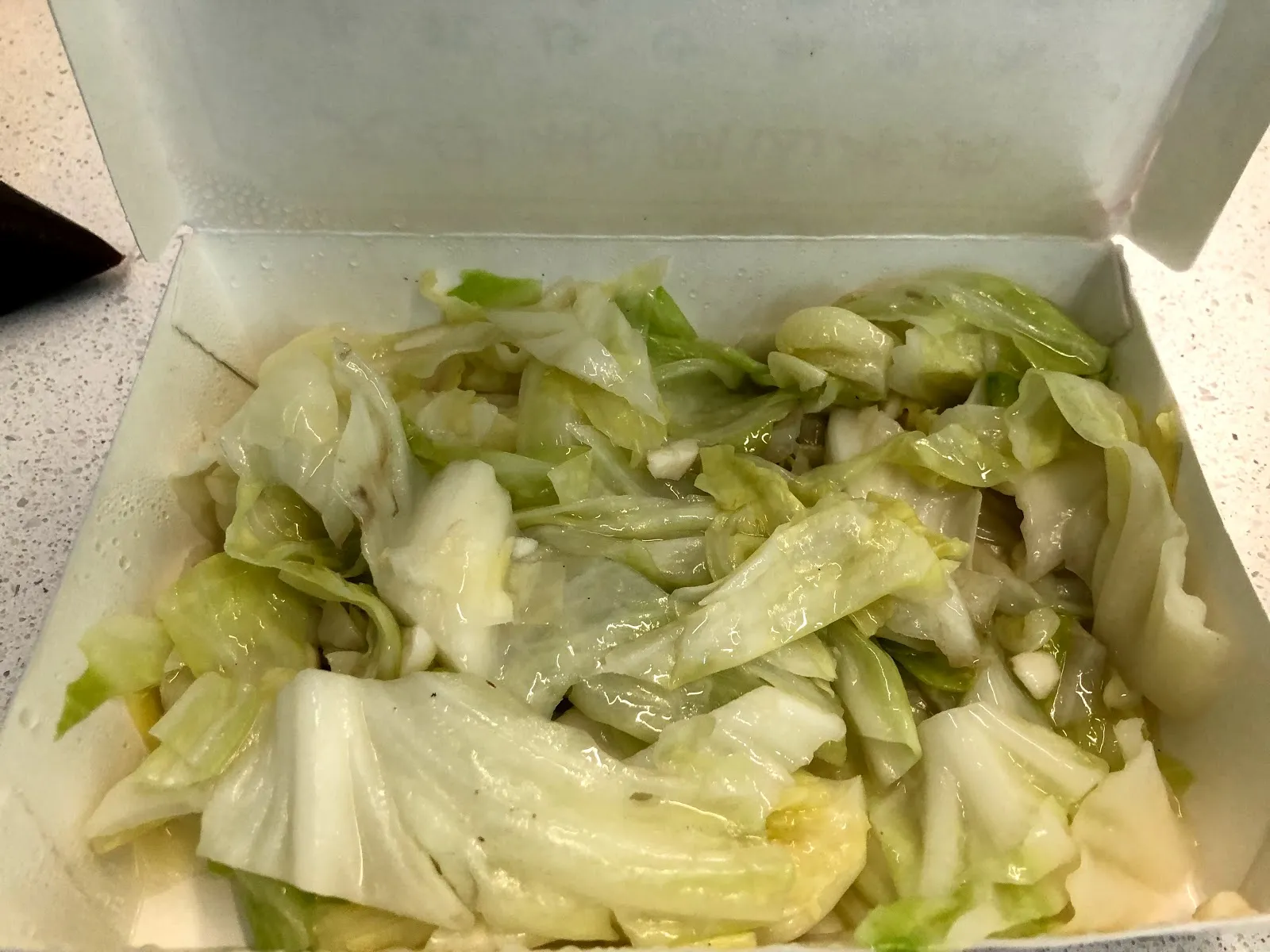 紙盒裡的炒高麗菜，菜葉炒得油亮透明，夾雜著蒜末