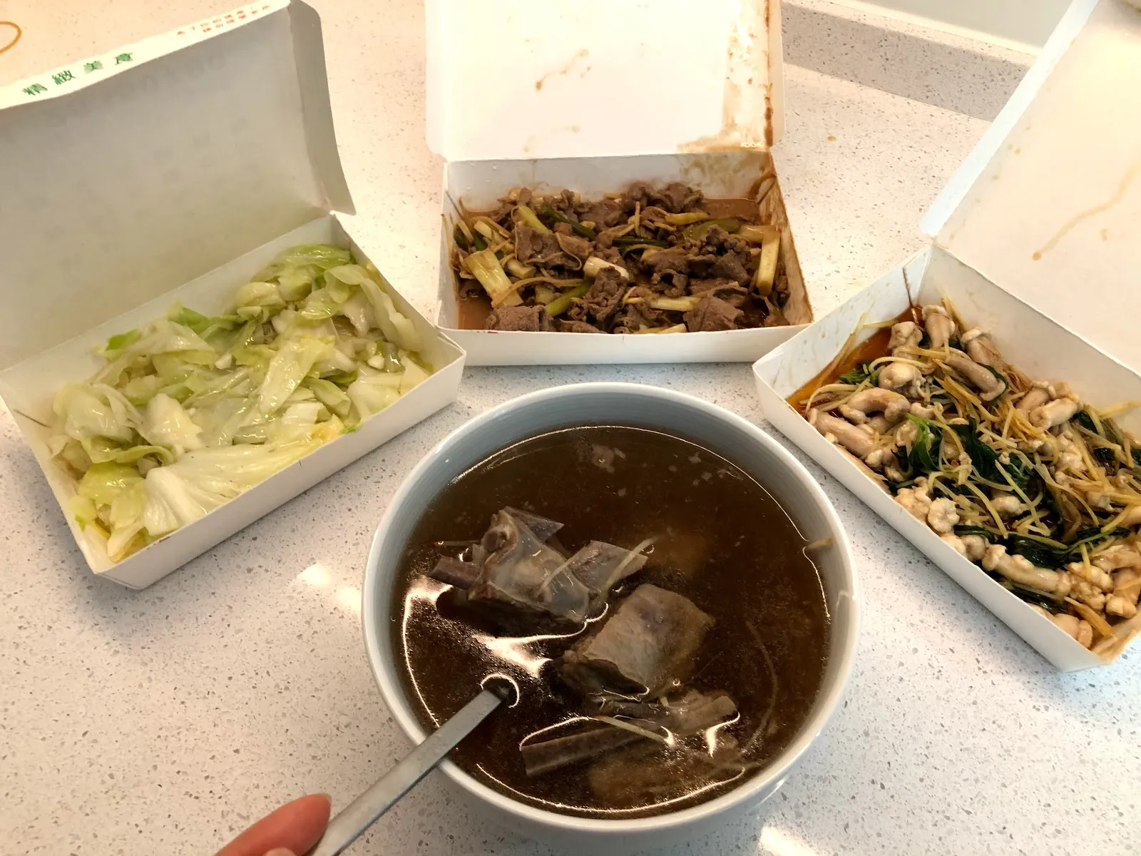 四樣外帶菜的另一角度，中央的羊肉湯碗裡浮著大塊帶皮羊肉，湯匙立在碗中