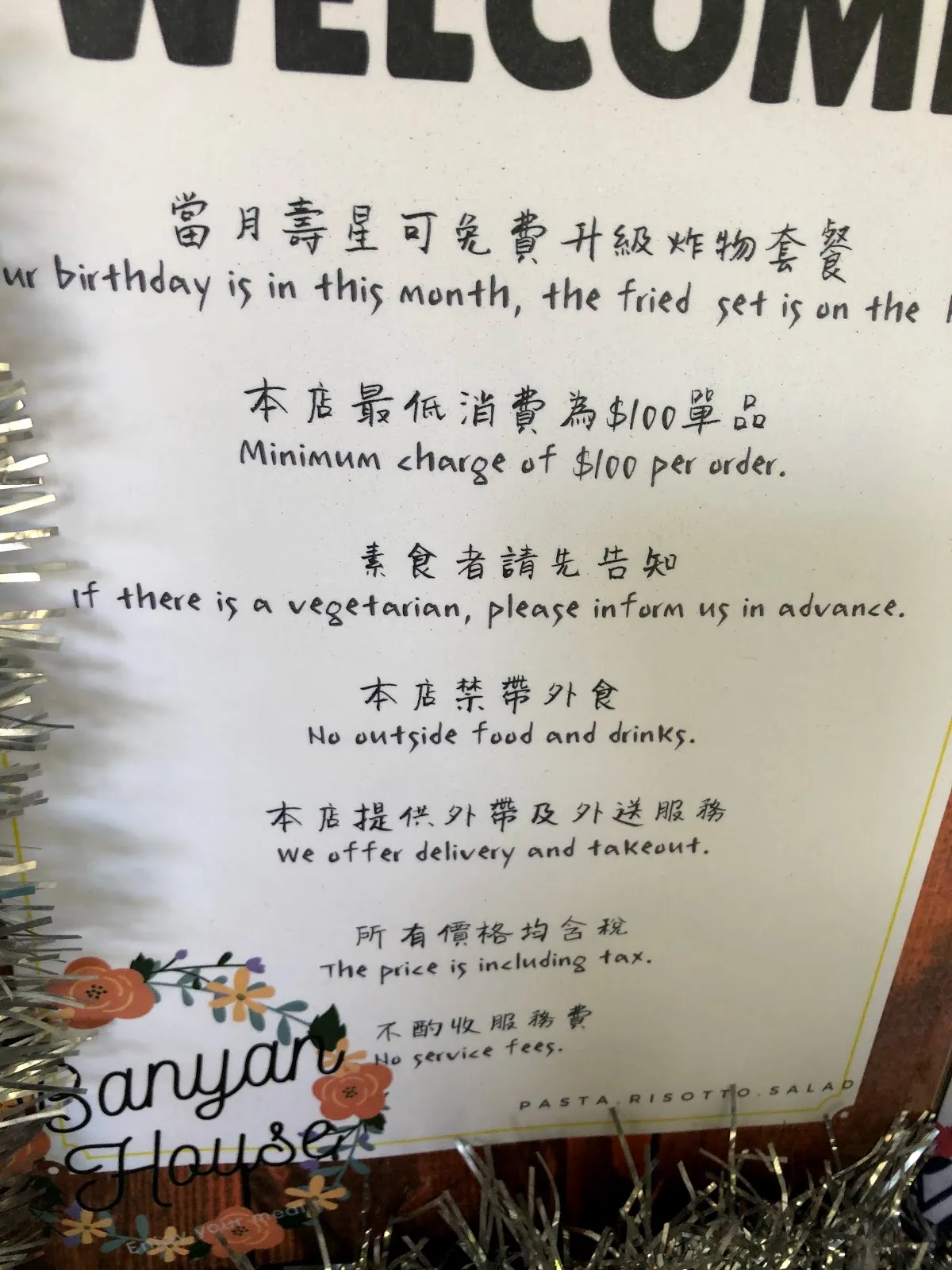 店內的告示牌，寫著當月壽星可免費升級炸物套餐、最低消費 100 元、不提供服務費，中英文對照