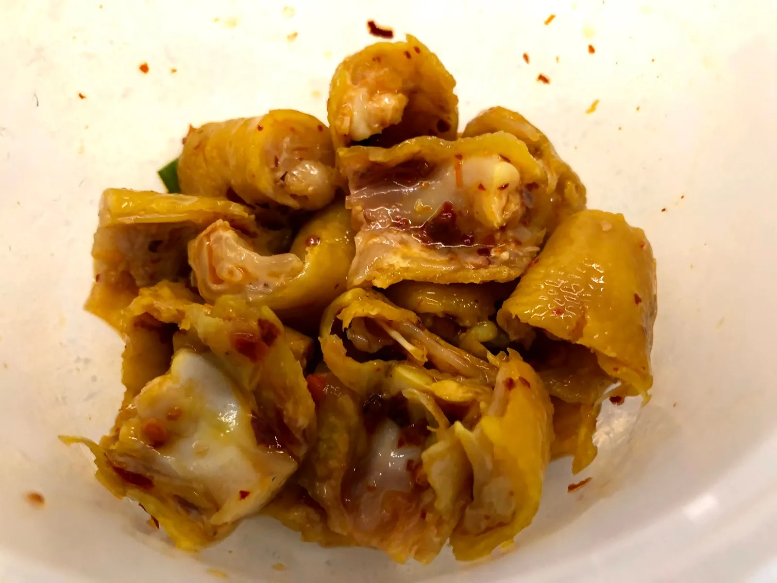 白色碗裡的雞骨與碎肉，淋著醬汁並撒上紅色辣椒碎