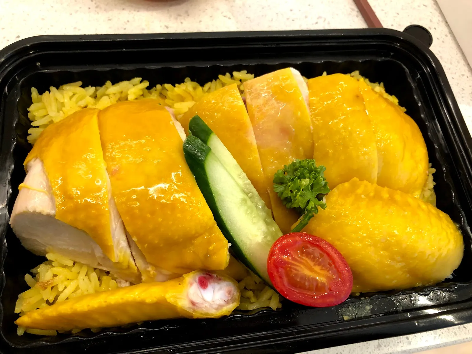 另一盒海南雞飯，油亮的雞腿肉切片鋪在黃色雞油飯上，中間插著小黃瓜片與番茄，旁邊還有一支雞翅