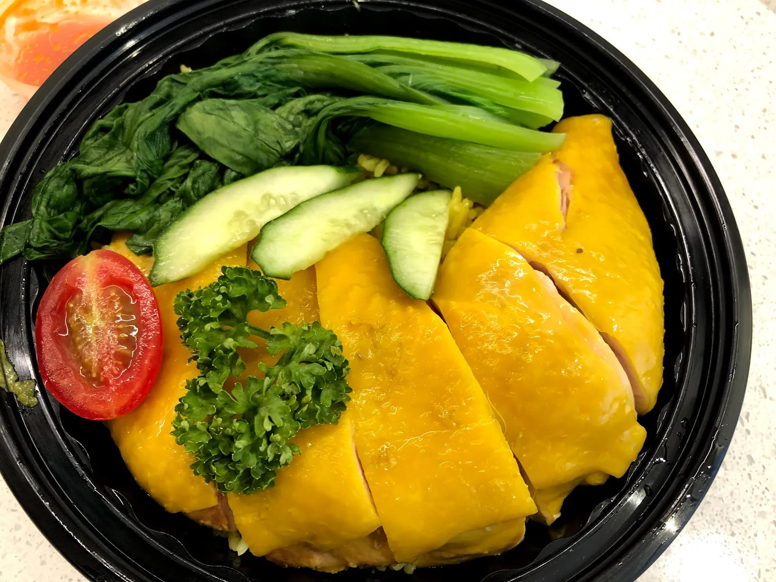 海南雞飯的俯拍，黃澄澄的去骨雞肉切片排在飯上，配上燙青菜、斜切小黃瓜、對半切的小番茄與一撮巴西里