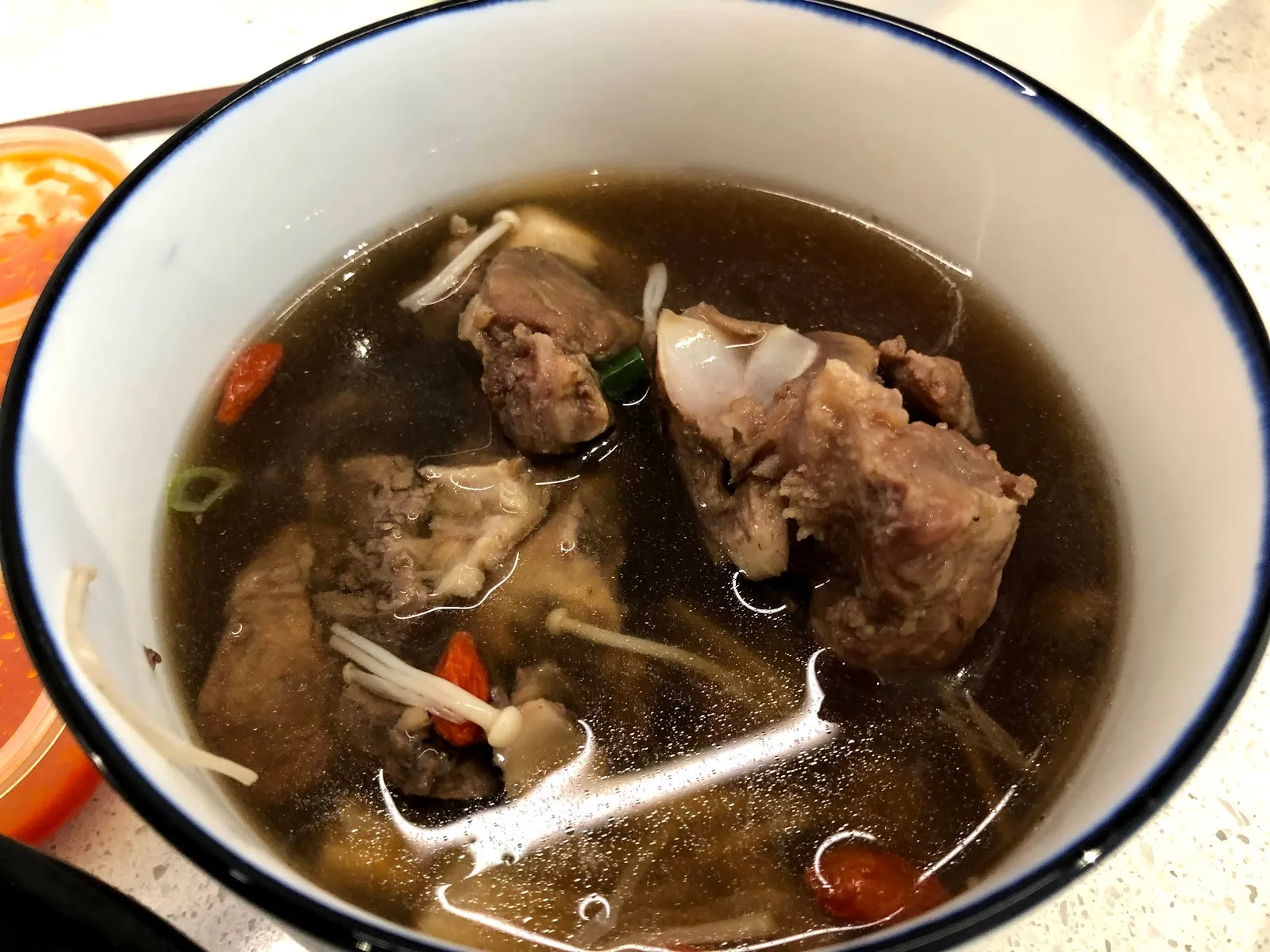白色湯碗裡的藥燉湯，深褐色湯汁中浮著排骨、金針菇與紅色枸杞