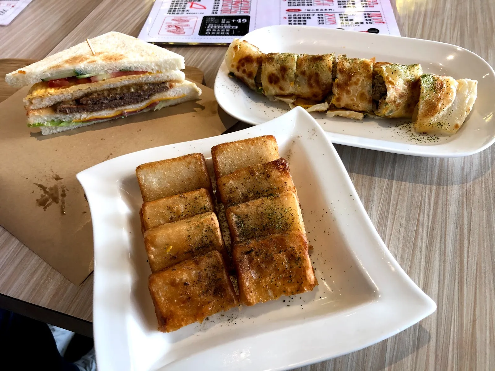 桌上的三份餐點：切開的三明治、蛋餅捲與一盤煎蘿蔔糕