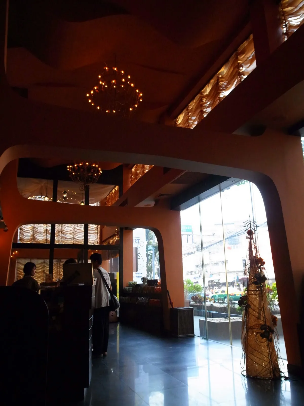 按摩店的迎賓大廳,橘色的曲面天花板與牆面嵌著金色燈飾,右側是整片落地窗與窗外街景