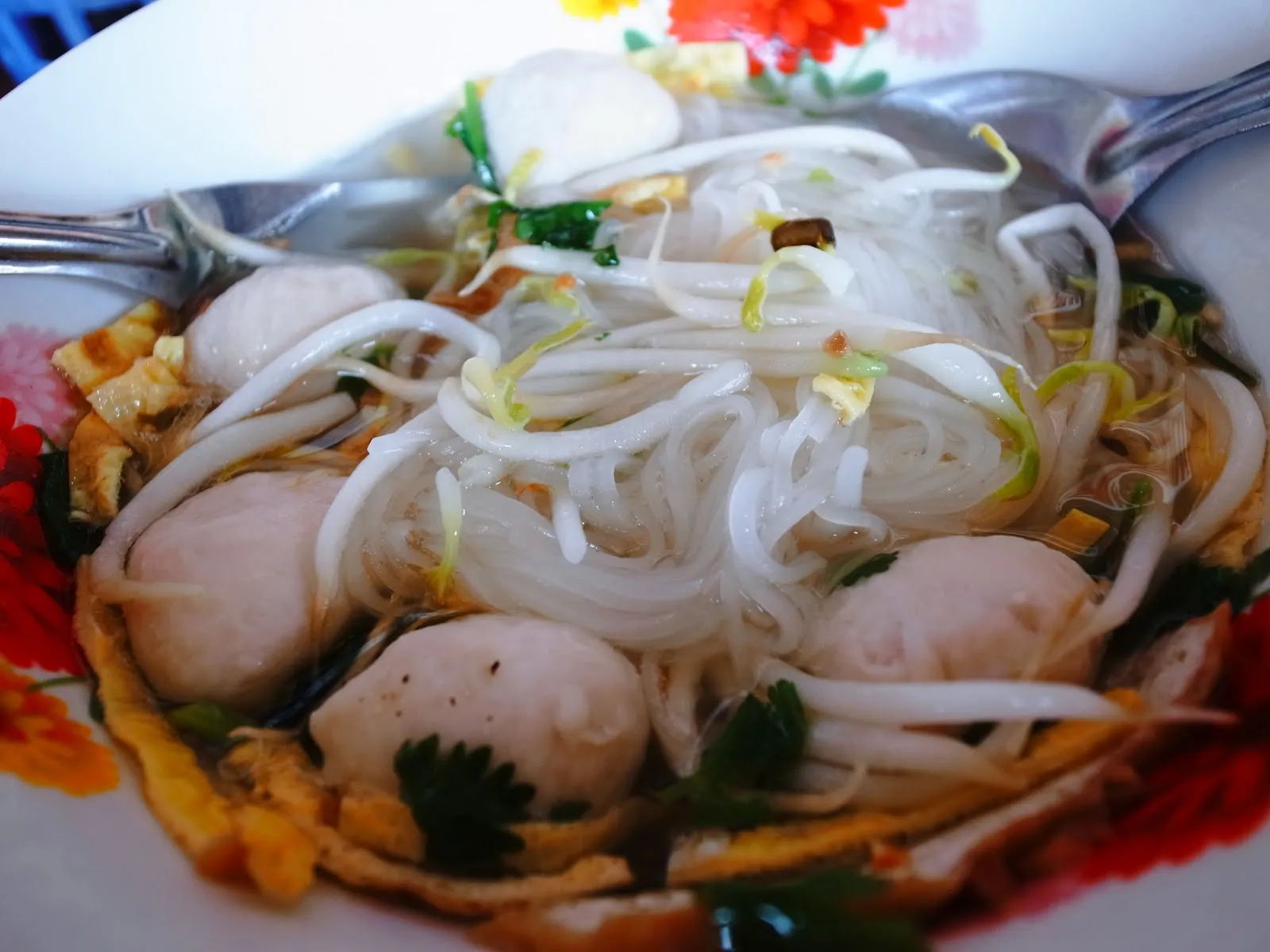 白盤裡的泰式米粉湯，粉條上放著魚丸、豆芽與香菜