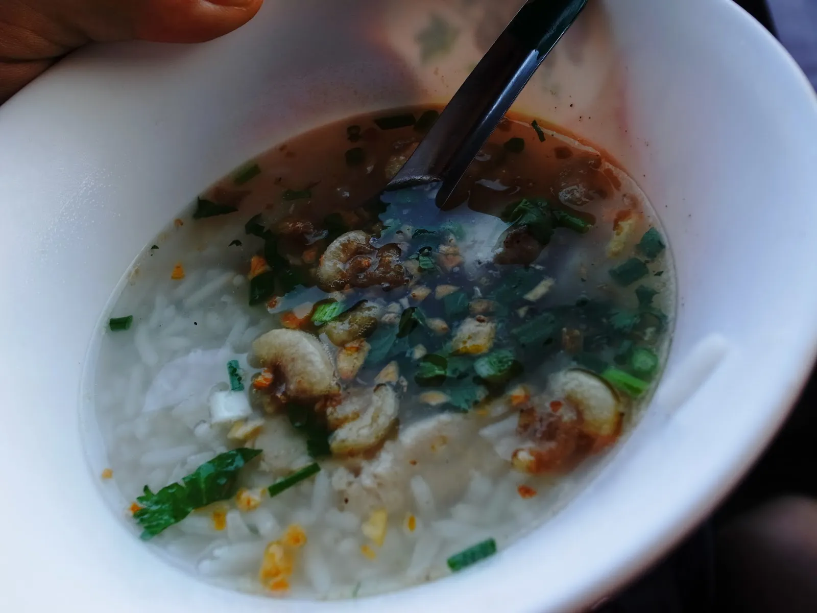 白色碗裡的泰式海鮮粥，粥裡有蝦仁、蔥花與香菜，插著一支湯匙
