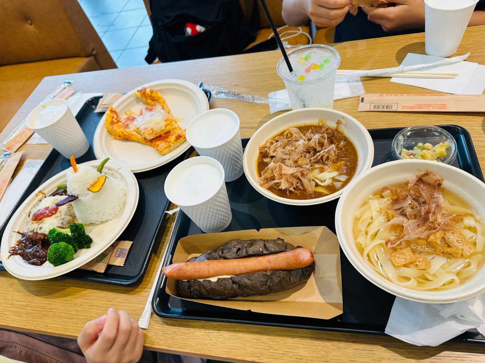 餐桌上擺滿餐點，有淋著醬汁的漢堡排飯、披薩、咖哩烏龍麵、清湯烏龍麵，以及一份夾著整條香腸的黑色麵包