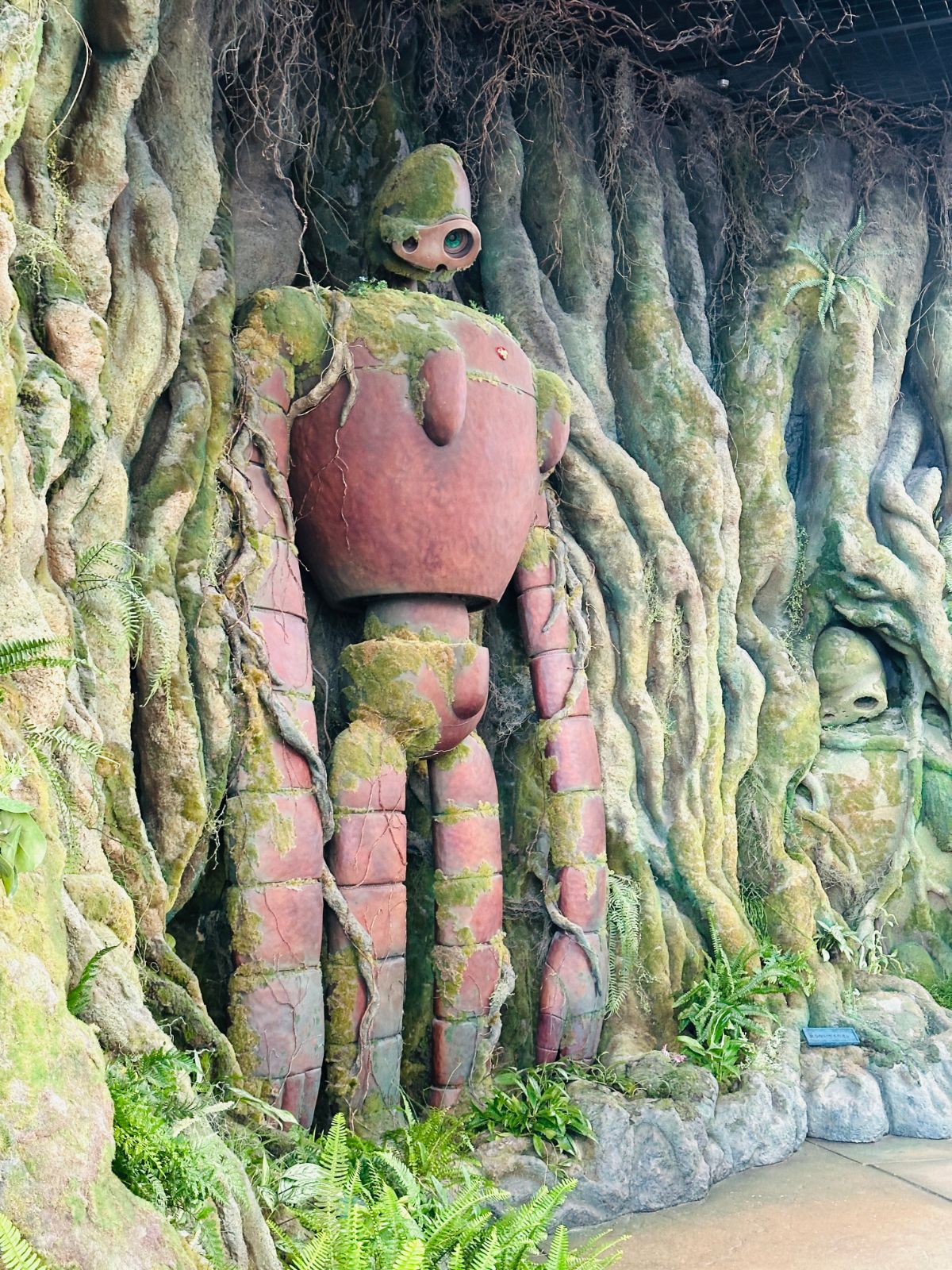 《天空之城》巨神兵的等身塑像,紅褐色的機械身軀爬滿青苔,佇立在垂著氣根的巨大樹牆前