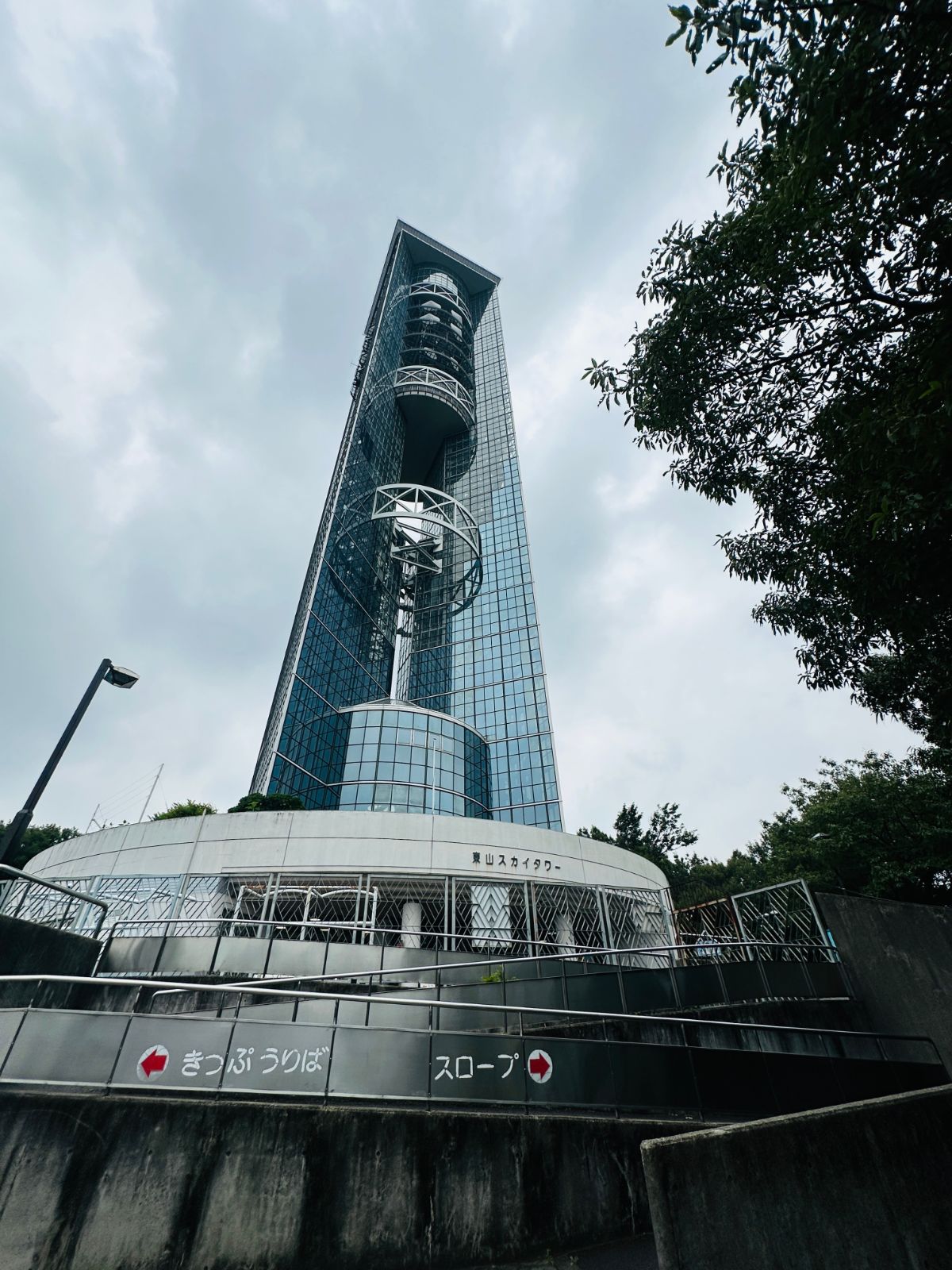 仰角拍攝的東山天空塔，玻璃帷幕的細長塔身直入陰天，底部是圓形的入口建築