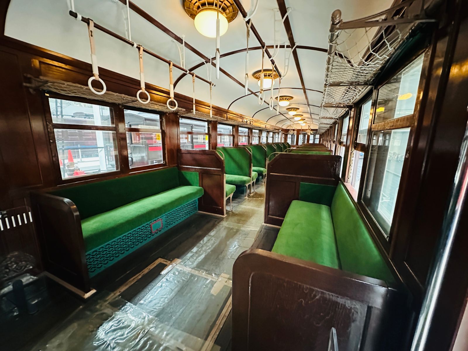 木造老車廂內部，兩側是綠色絨布長椅，天花板垂下一排白色吊環，行李架是網狀的