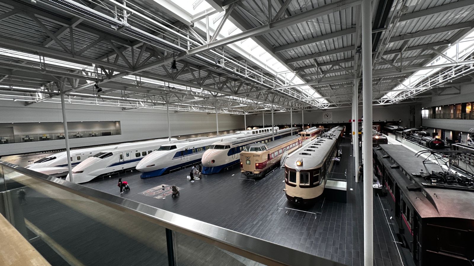 從高處俯瞰整個展示大廳，白色新幹線、橘色電車與深紅色路面電車依序排列