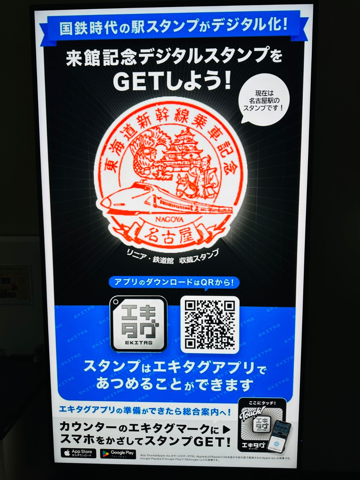 館內的數位紀念章看板，中央是東海道新幹線乘車紀念的橘紅色印章圖案，下方有下載 EKITAG 應用程式的 QR code