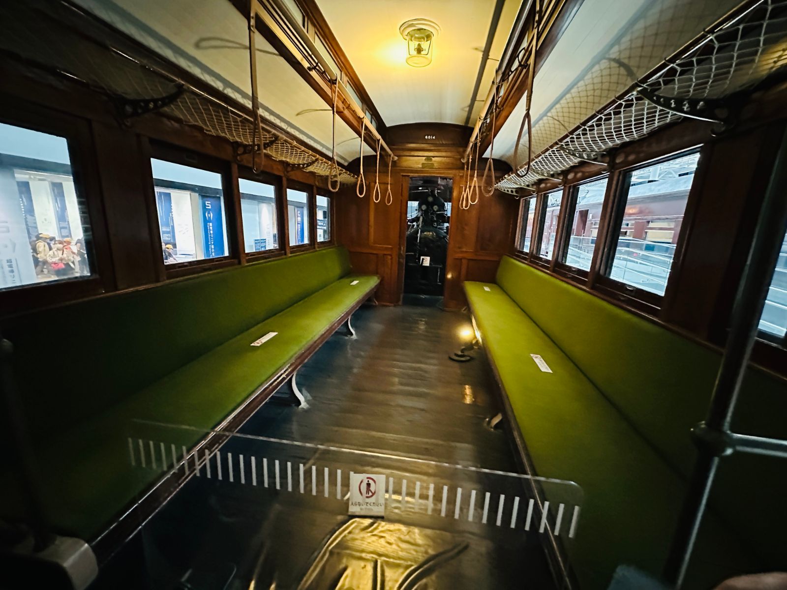 另一節木造車廂，橄欖綠長椅沿兩側排開，深色木頭牆面與圓形吊燈，盡頭是駕駛室