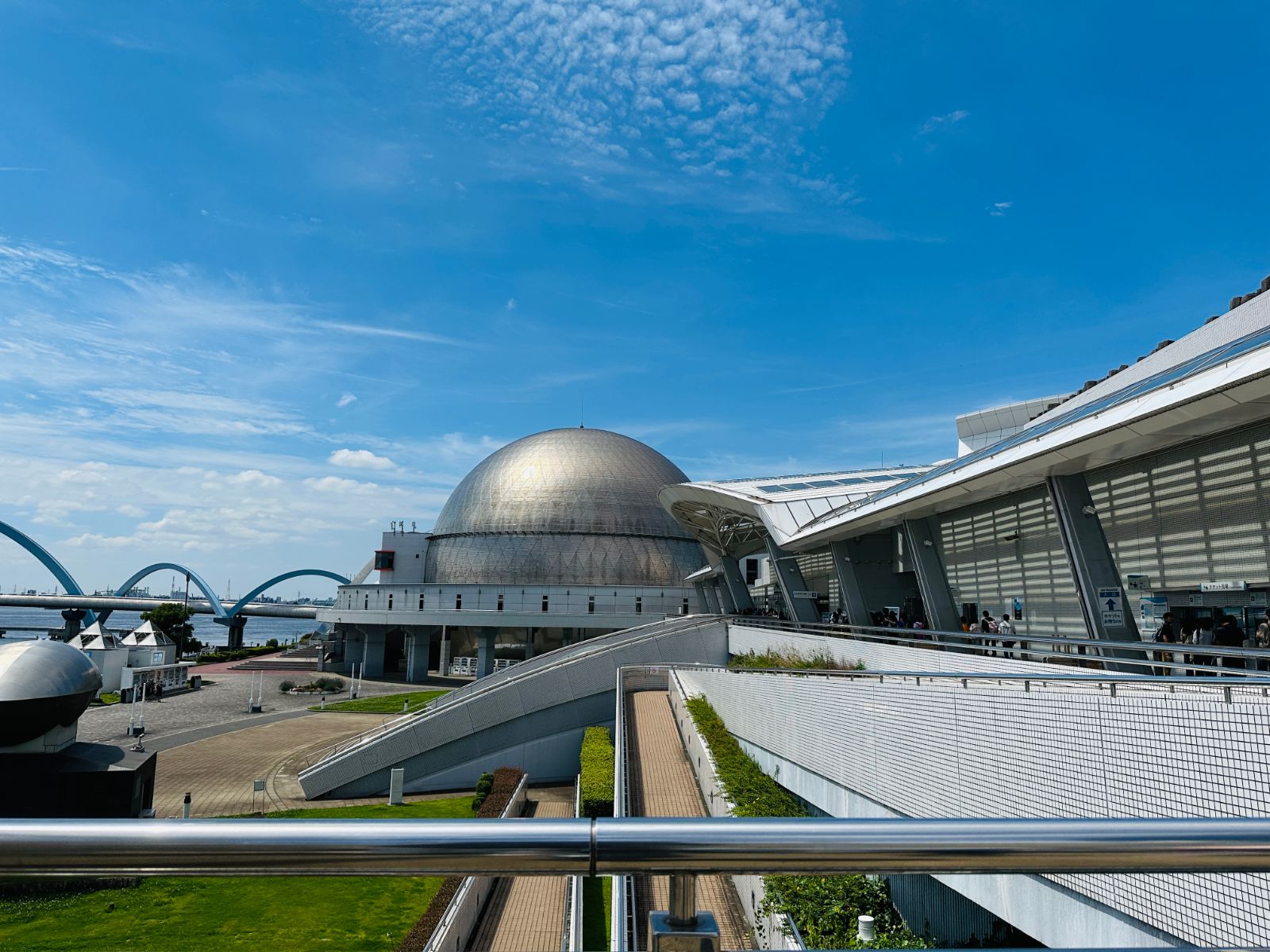 水族館的銀色圓頂建築外觀,一旁是白色的弧形通道與遠處的紅色跨港大橋